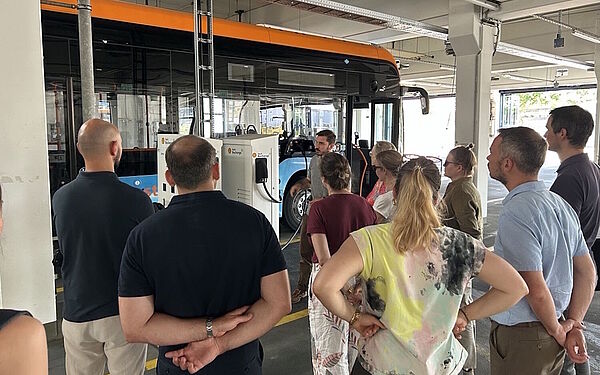 Personen besichtigen den Betriebshof der rnv in dem ein BZ-REX-Bus an einer Ladesäule steht